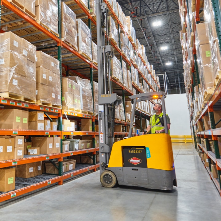 man using standing forklift to get box from top of rack shelves
