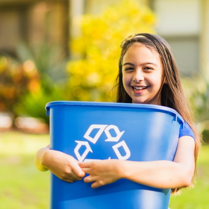young girl smiling and holding a blue recycle bin